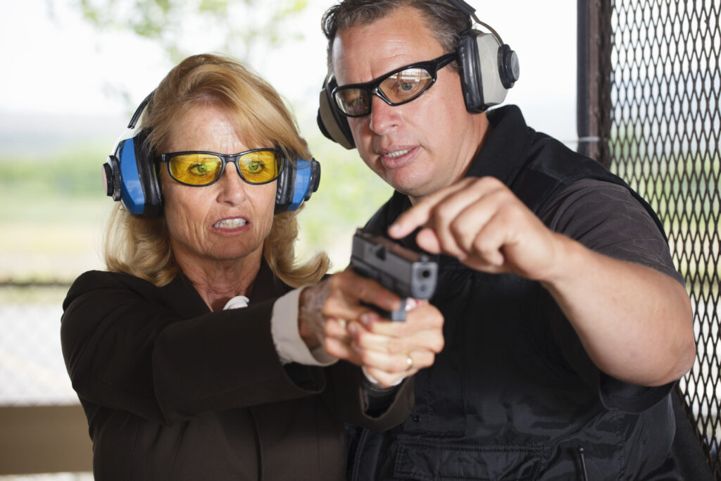 A firearm shooting instructor assisting a student at a shooting range.